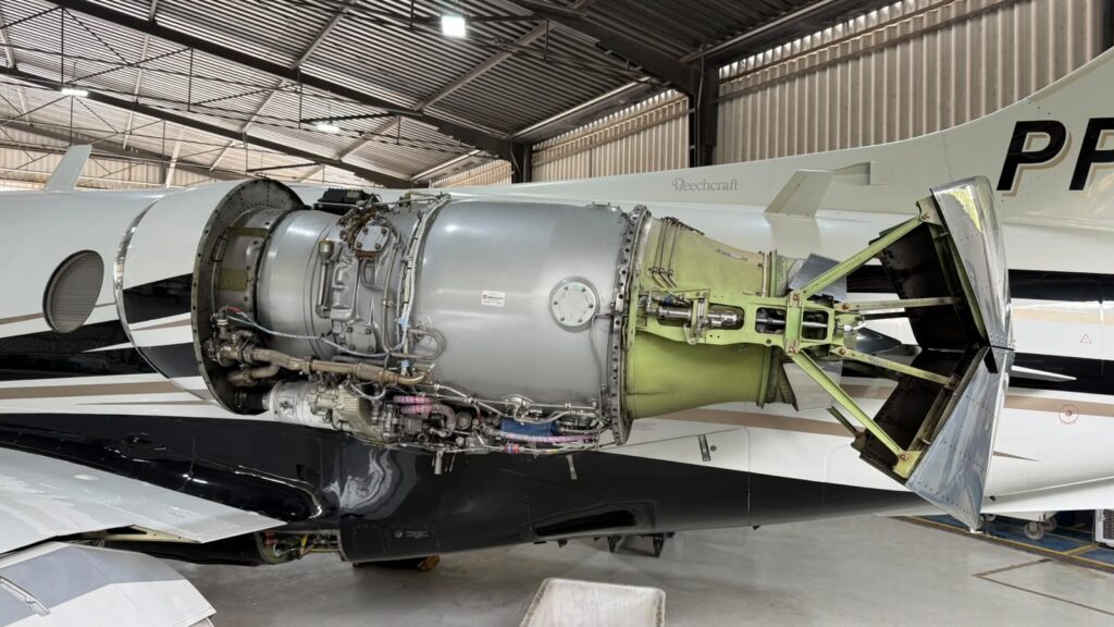 Vista lateral de um avião em manutenção, com o motor a jato exposto e a área da fuselagem aberta em oficina hangar industrial
