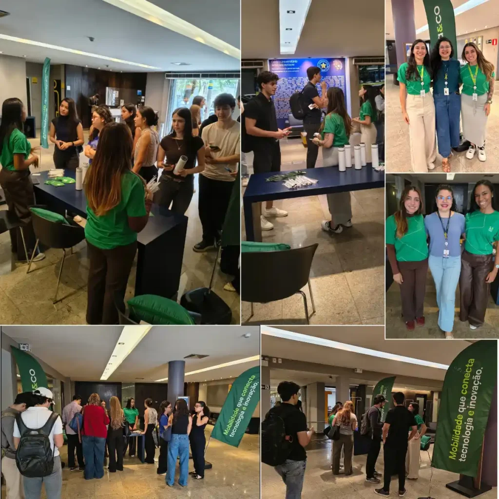 Pessoas participando de um evento em um hall, com mesas de credenciamento, banners verdes e dois grupos de participantes posando para fotos. Ambiente interno, palestras e interação.