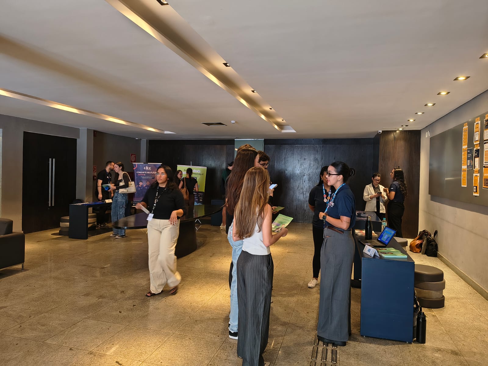 Recepção em evento corporativo com participantes e equipe em um espaço interno moderno, balcões de atendimento e iluminação embutida no teto.
